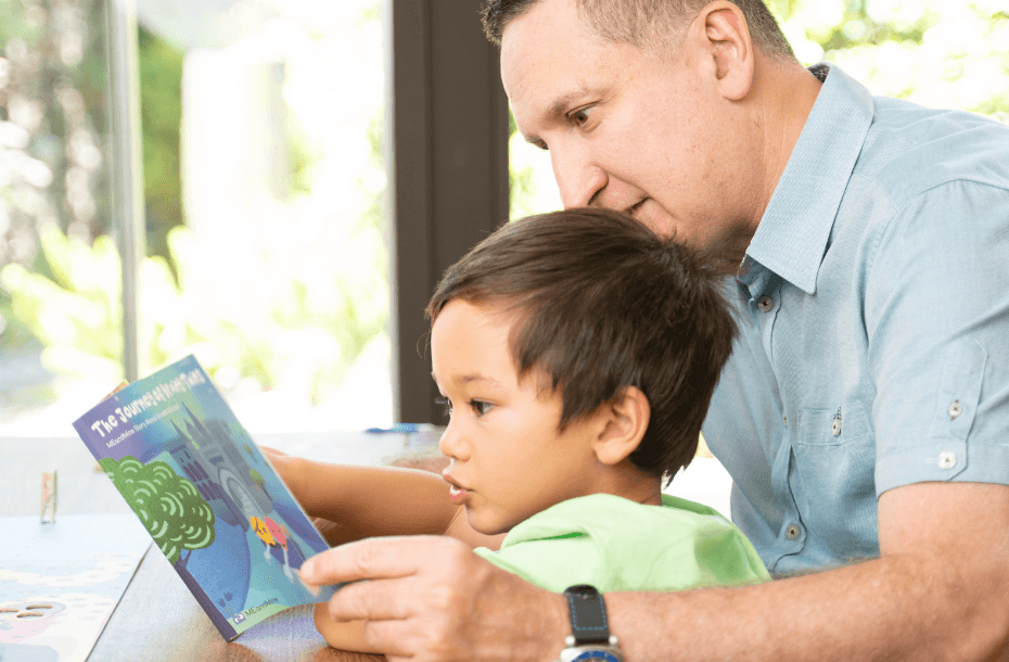 A father and his young son look together at a MEandMine storybook titled The Journey of Brave Twins.