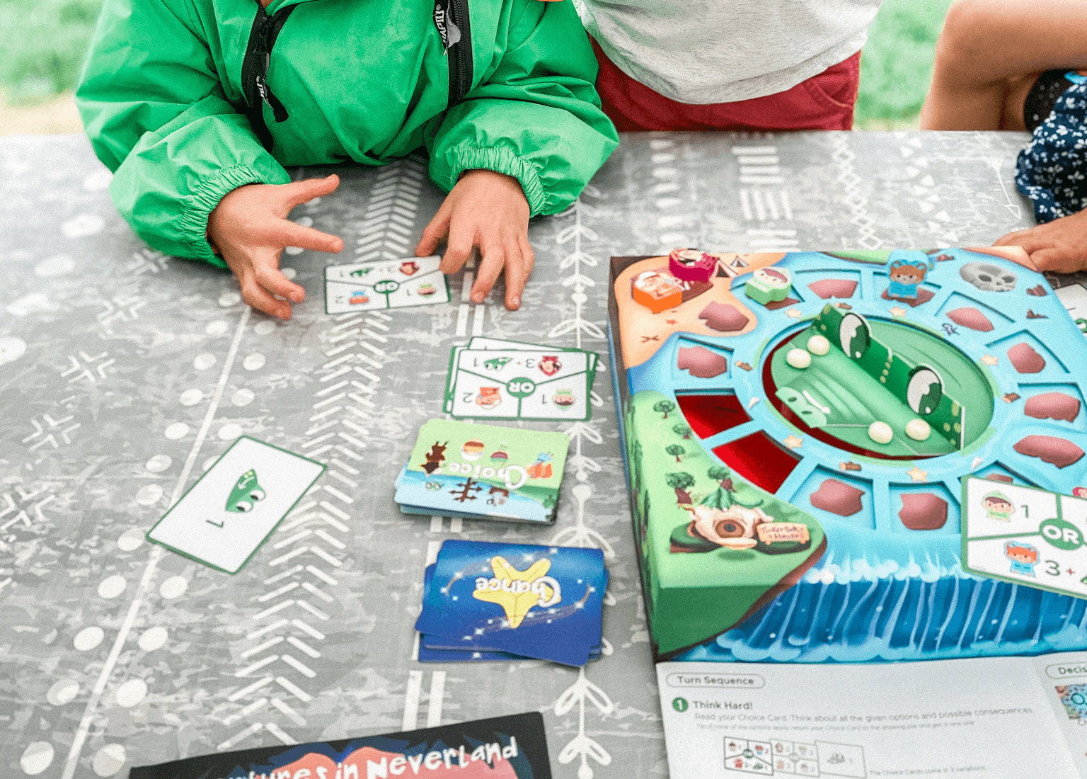 Children's hands lay out choice cards beside the Aha! Decision Making Adventures in Neverland board game