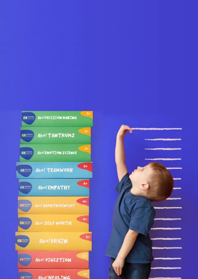 A boy reaching up a height chart beside a tower of Aha! play kit boxes