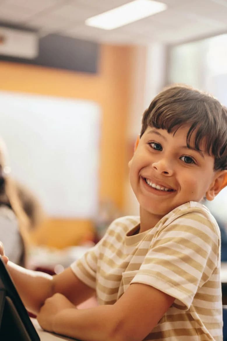 A smiling boy at a tablet in a classroom