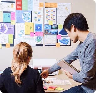 Two educators planning at a desk in front of a wall of notes