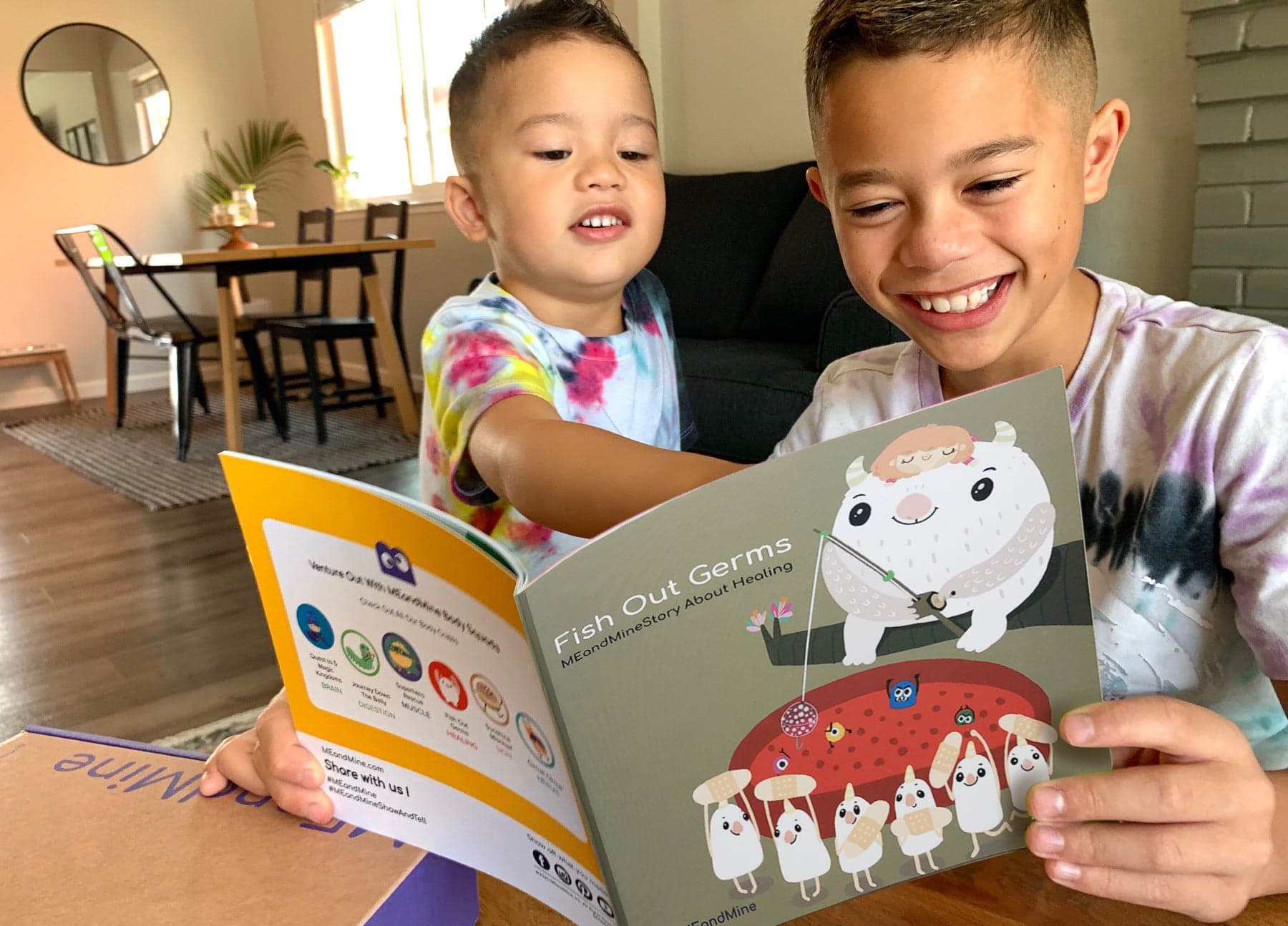 Two smiling boys read the MEandMine storybook Fish Out Germs, with a white monster fishing above bandage characters.