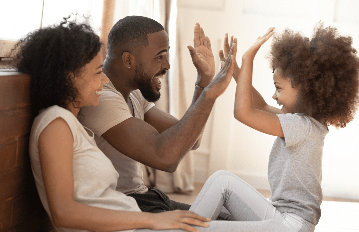A smiling father and daughter high-five while the mother sits beside them laughing.