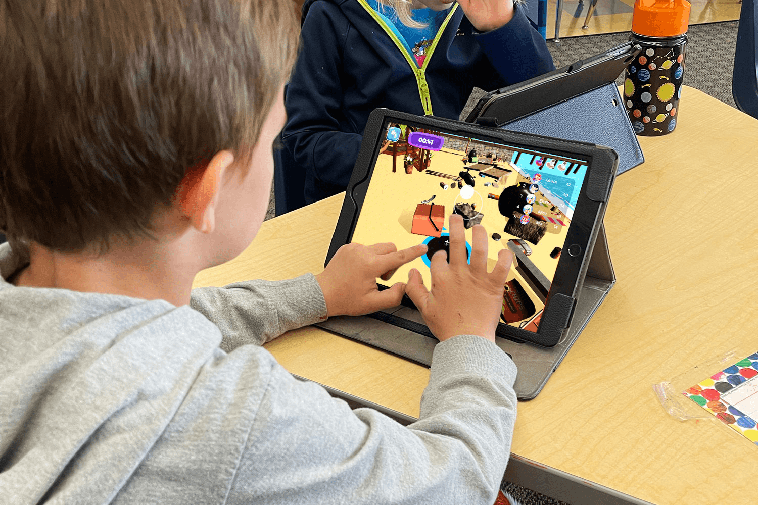A boy plays a 3D game on a tablet in the MEandMine app at a classroom desk, with a countdown timer and scoreboard on screen.